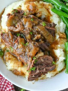 a white plate topped with mashed potatoes covered in beef and gravy next to green beans