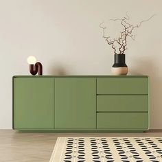 a green cabinet sitting on top of a wooden floor next to a vase filled with flowers