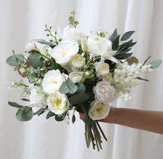 a person holding a bouquet of white flowers and greenery in front of a curtain