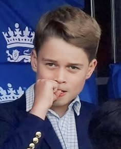 a young boy wearing a blue suit and holding his hand to his face while looking at the camera