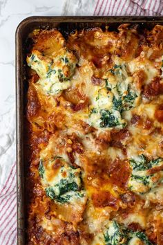 a casserole dish with spinach, cheese and meat in it on a red and white towel