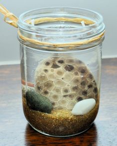 a jar filled with rocks and sand on top of a wooden table