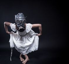 a woman wearing a gas mask and white dress with her hands on her hips while standing in the air