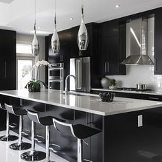 a large kitchen with black cabinets and white flooring is pictured in this image, there are four bar stools at the center of the island