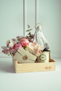 a wooden box filled with flowers next to a white statue and card holder on top of a table