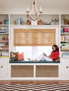 a woman sitting on a window seat in front of a book shelf filled with books