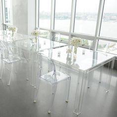 a dining room table with clear chairs and flowers in vases on the end tables