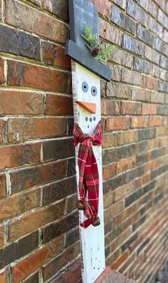 a wooden snowman with a red scarf hanging on the side of a brick wall