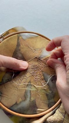 two hands are stitching together fabric on a small round bag that is sitting on a table