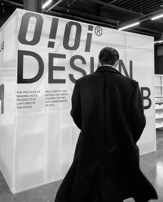 a man in a black coat is walking by a large white sign with the words design on it