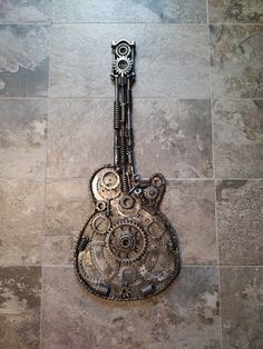 a guitar made out of metal parts sitting on top of a tile floor next to a wall