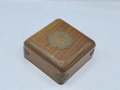 a small wooden box with a gold emblem on the lid sitting on a white surface