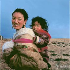 a woman carrying a child on her back in an open area with grass and blue sky