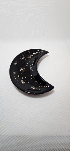 a black and gold crescent shaped brooch on a white surface with small speckles