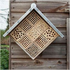 a square shaped wooden object hanging on the side of a building with holes in it