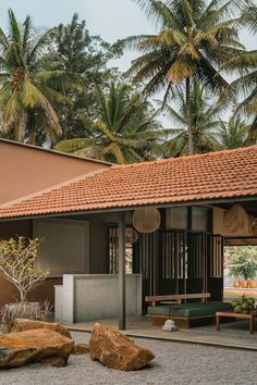 an outdoor area with rocks and trees in the foreground, near a building that has a red tiled roof