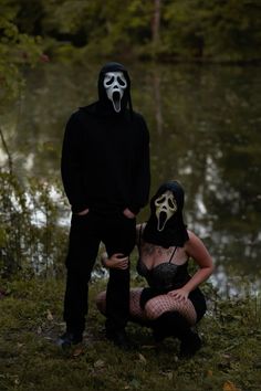 two people wearing masks standing next to each other in front of a body of water