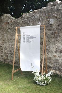 a white sign sitting in the grass next to a stone wall