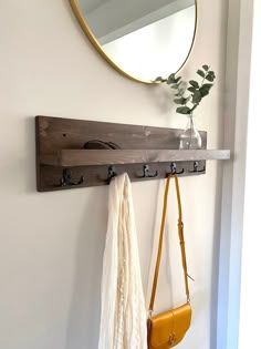 a coat rack and mirror hanging on the wall next to a yellow purse with two hooks