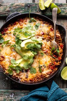 a skillet filled with mexican food and garnished with avocado, cilantro, and lime