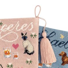 two cross - stitch books with tassels on them, one in pink and the other in blue