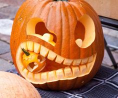 a carved pumpkin sitting on top of a table next to another pumpkin with it's mouth open