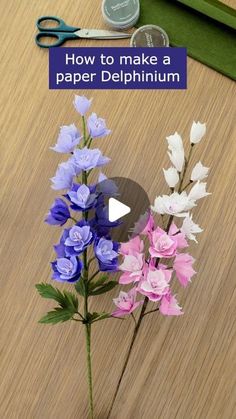 a vase filled with purple and white flowers on top of a wooden table next to scissors