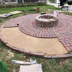 a brick fire pit in the middle of a yard with grass and other items around it