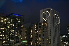 the city skyline is lit up at night, with buildings in the foreground and an illuminated smiley face on the building