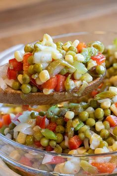 a wooden spoon filled with mixed vegetables on top of a glass bowl full of peas and carrots