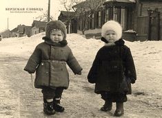 two children are walking in the snow holding hands and wearing winter clothes with fur on them