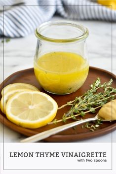 a plate with lemons, herbs and a jar of liquid on it next to a knife