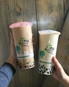 two people are holding up their drinks in front of a wooden wall with the words tea on it