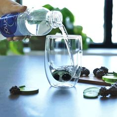 a person pouring water into a glass filled with blackberries and cucumber slices