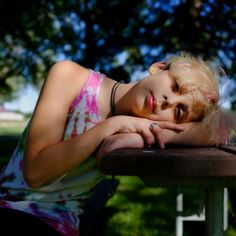 a woman with blonde hair laying on top of a wooden table next to a tree