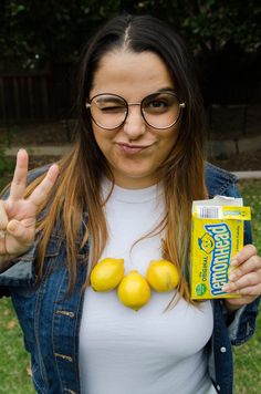 a woman with glasses holding up two lemons and a carton of juice in front of her