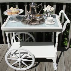 a white table topped with a tray filled with cupcakes next to a silver tea pot