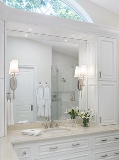 a large bathroom with white cabinets and marble counter tops is pictured in this image, there are flowers on the sink