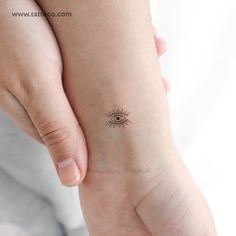 a small tattoo on the wrist of a woman's left hand, depicting an eye