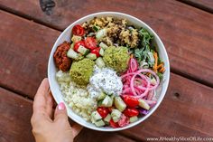 a person is holding a bowl full of food on a wooden table with wood planks