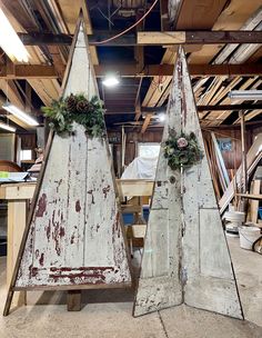 two white wooden christmas trees with wreaths on them in an unfinished warehouse area,