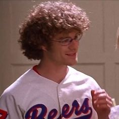 a man with curly hair wearing a baseball uniform and holding a drink in his hand