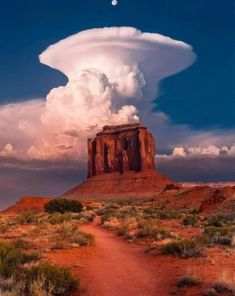 a large cloud is in the sky over a desert area with a dirt path leading to it