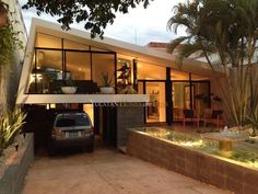 a car is parked in front of a house with large windows and plants on the outside