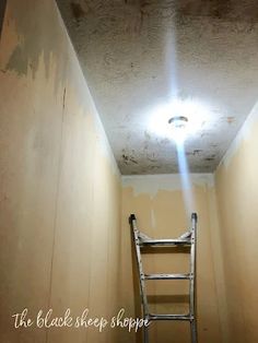 a ladder going up the side of a wall in an empty room with light coming from above