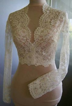 a mannequin wearing a white lace top with long sleeves and an open back