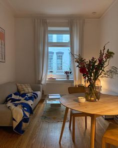 a living room filled with furniture and a wooden table next to a window on top of a hard wood floor