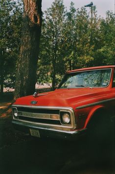 an old red car parked next to a tree