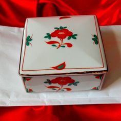 a white box with red flowers on it sitting on a tablecloth covered surface,