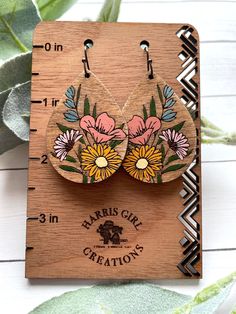 a pair of earrings with flowers on them sitting on top of a piece of wood